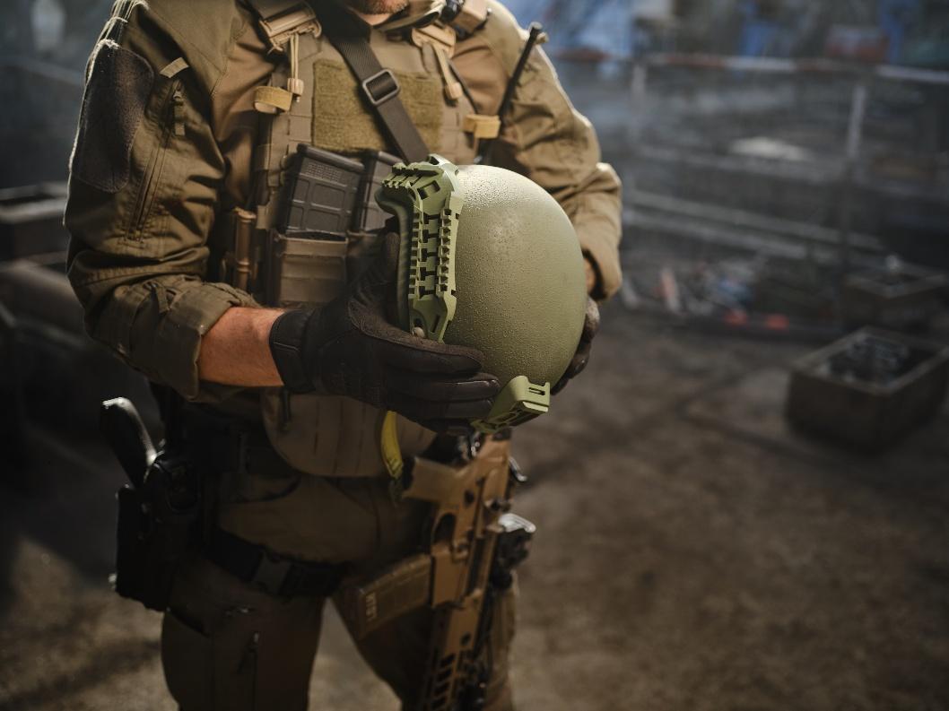 Soldier in tactical gear holding a seamless one-piece ballistic helmet shell with side rails